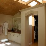 Portal into master bath with sink area beyond and shower,  Ridge skylights fly above and beyond into dressing hall providing balanced light deep into the spaces.